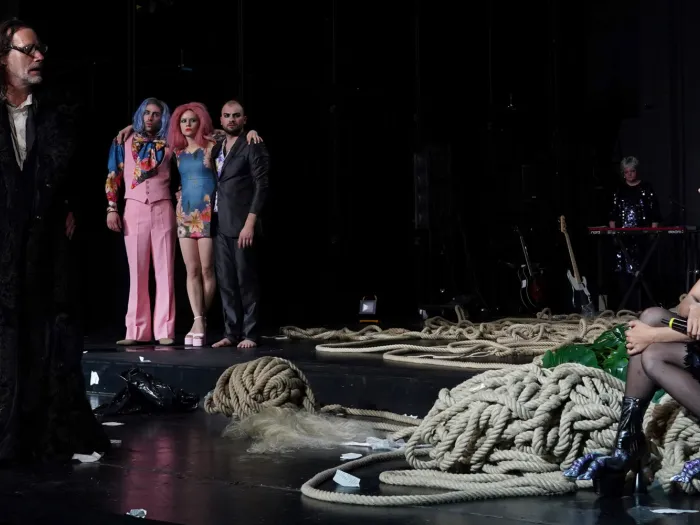 Szene aus "Der Sturm", 2022 im Theater am Kornmarkt, sechs kostümierte Darstellende, ein Mann mit schwarzem Pelzmantel, eine sitzende Frau mit grauem Haar und schwarzem Paillettenkleid, auf der Bühne liegen Seile