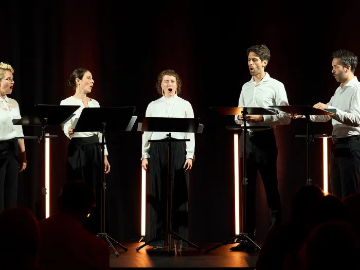 Szene aus "Konzert im KUB", 2024 im Kunsthaus Bregenz, fünf Sänger:innen mit weißem Hemd und schwarzer Hose, stehend hinter je einem Pult