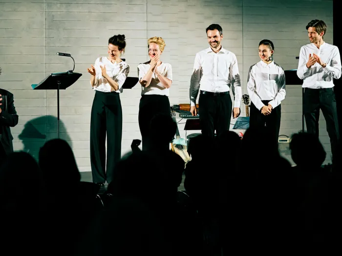 Szene aus "Konzert im KUB", 2021 im Kunsthaus im KUB, sieben Personen in formeller Kleidung, zwei davon in dunkler Kleidung, Publikum im Vordergrund