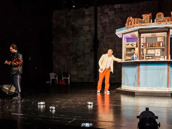 Szene aus "Lohn der Nacht", 2021 im Theater Kosmos, drei kostümierte Darstellende, Kiosk mit Darstellerin, vier Flaschen auf dem Boden