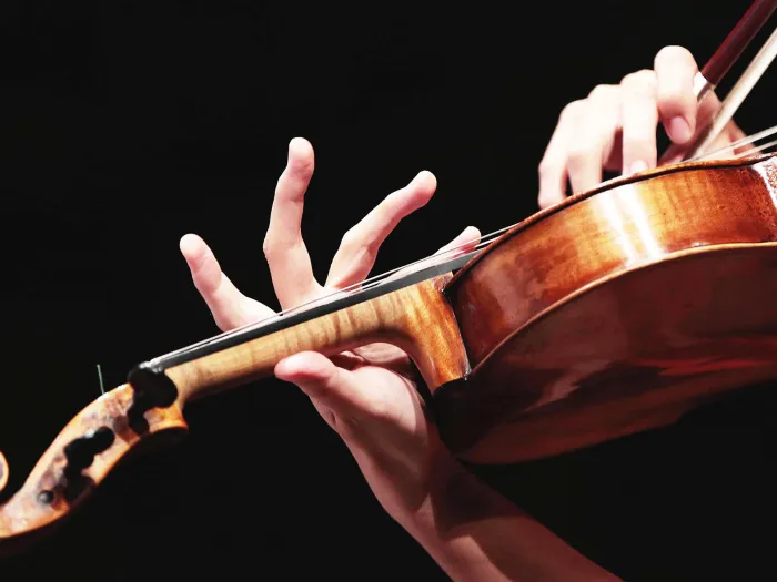 Detailaufnahme Geige, rechte Hand setzt den Bogen an, linke Hand greift den Hals des Instruments