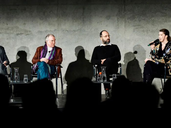 Szene aus "Einblick 1", 2022 im Kunsthaus Bregenz, vier Personen auf der Bühne, sitzend vor Publikum, rechts eine hängende Geige