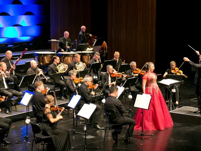 Szene aus "Viva Verdi - Viva L'Opera", 2020 im Festspielhaus, Musikerinnen auf der Bühne, Sängerin in rotem Kleid singt zentral