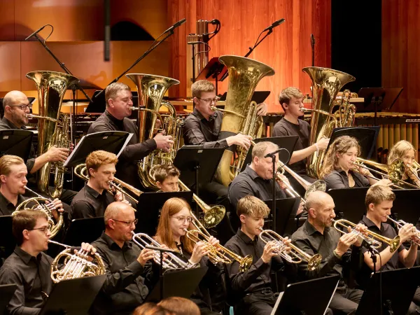 Eine Gruppe von Musikern in schwarzer Kleidung spielt Blechblasinstrumente, darunter mehrere Tubas und Trompeten, auf einer Bühne.